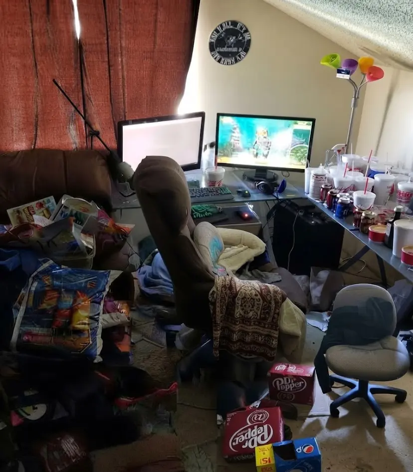 Panoramic view of Asmongold's room filled with fast-food cups, soda boxes, messy chairs, and dual monitors on a glass desk.